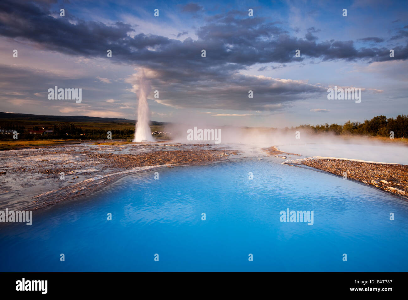L'Islande, Geysir, rising sun lights Deep blue piscine thermale et de la vapeur à partir de la ventilation Strokkur Geyser sur matin d'été Banque D'Images