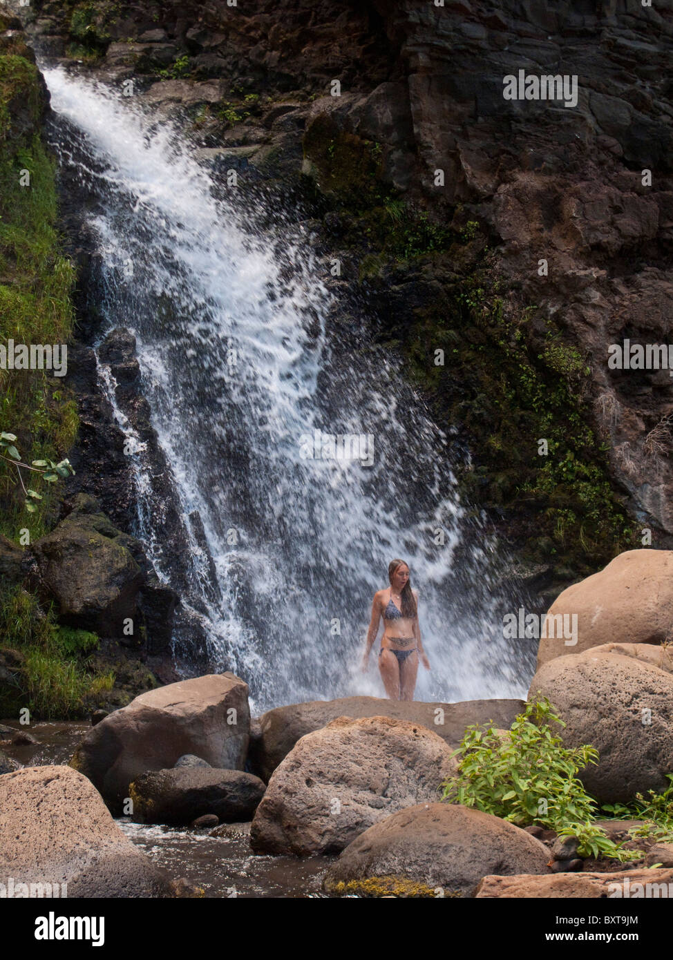 Femme debout sous une grande cascade de Honopu Valley près de la côte Napali, Kauai Banque D'Images