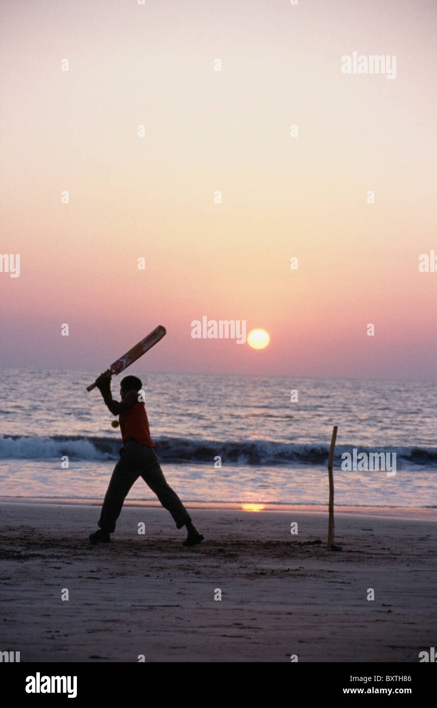 L'homme à jouer au cricket sur la plage au coucher du soleil Banque D'Images