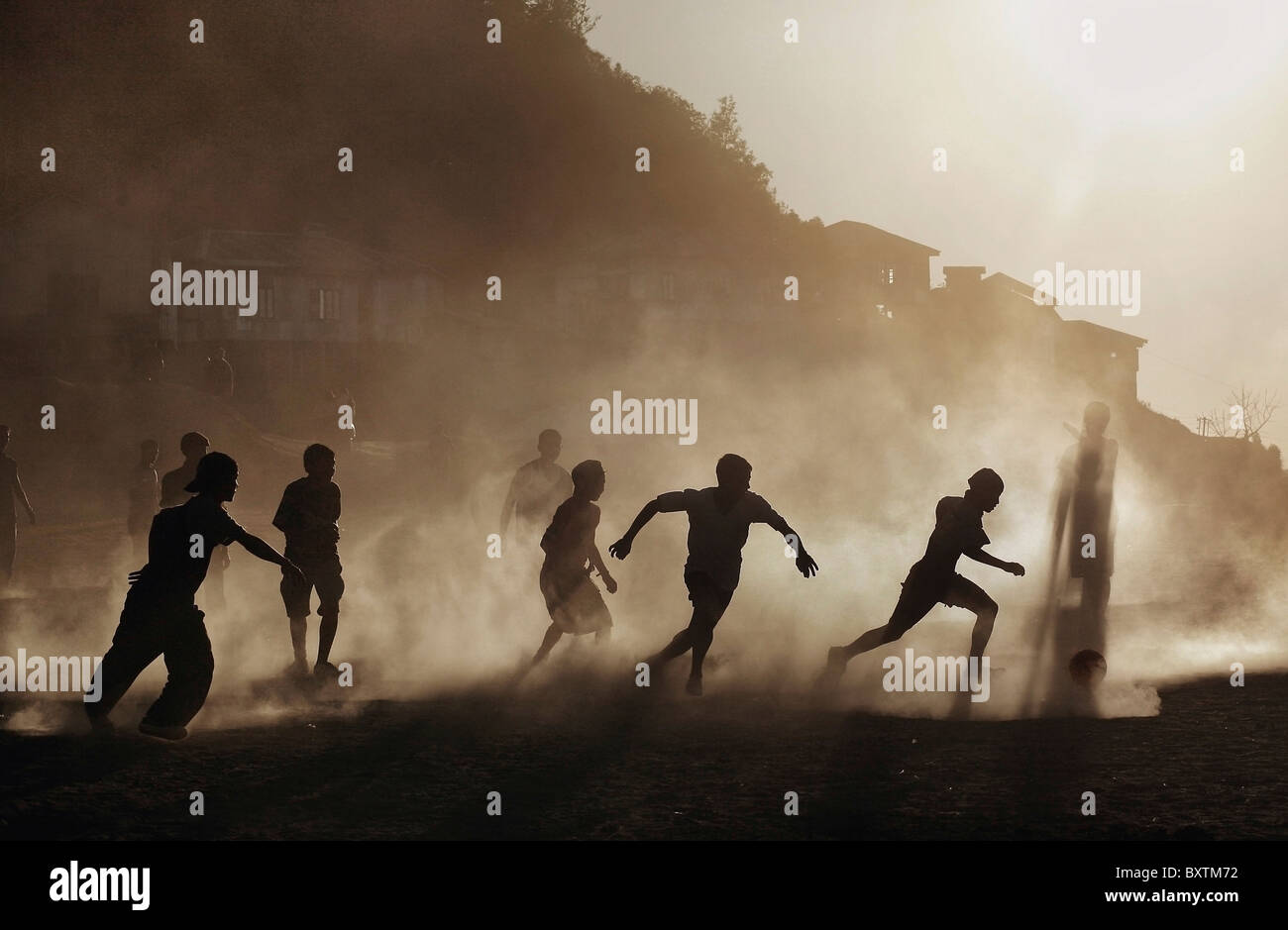 Silhouettes de garçons Mizo exécuté sur un terrain de soccer poussiéreux au coucher du soleil Banque D'Images