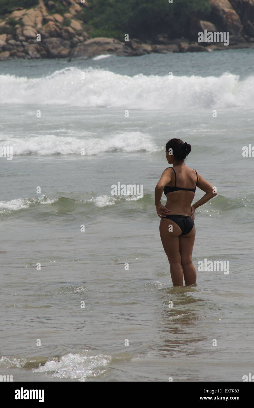 Young Caucasian woman wearing bikini de patauger dans l'eau à la plage de l'avant Banque D'Images
