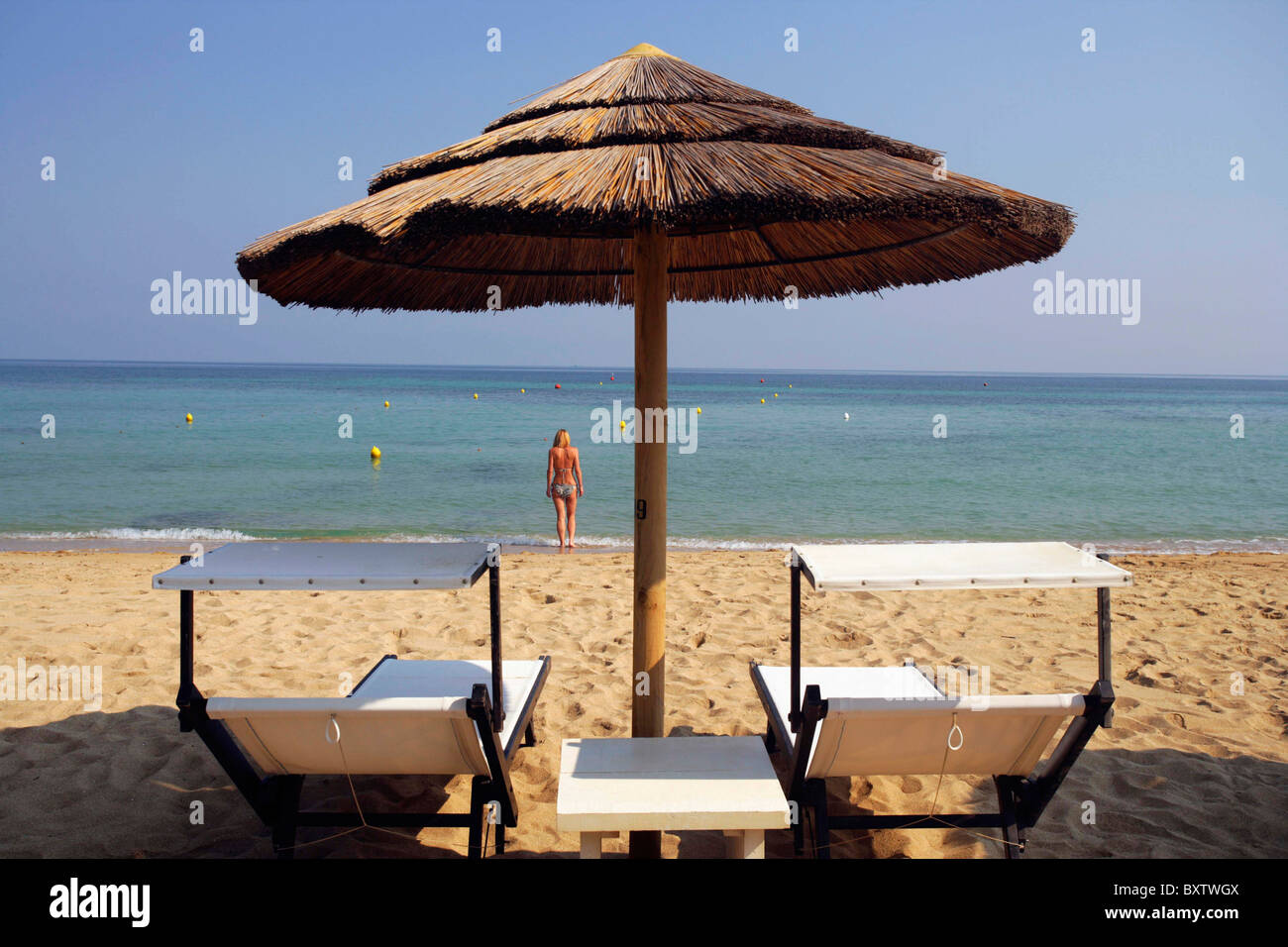 Vide Chaises Longues et parasol au toit d'herbe avec femme debout derrière la mer en Banque D'Images