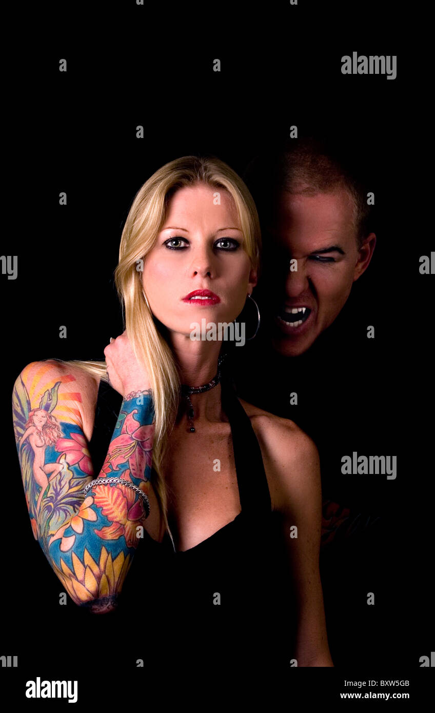 Homme vampire en arrière-plan foncé furtivement vers le haut sur les attractive blonde femme tatouée Banque D'Images