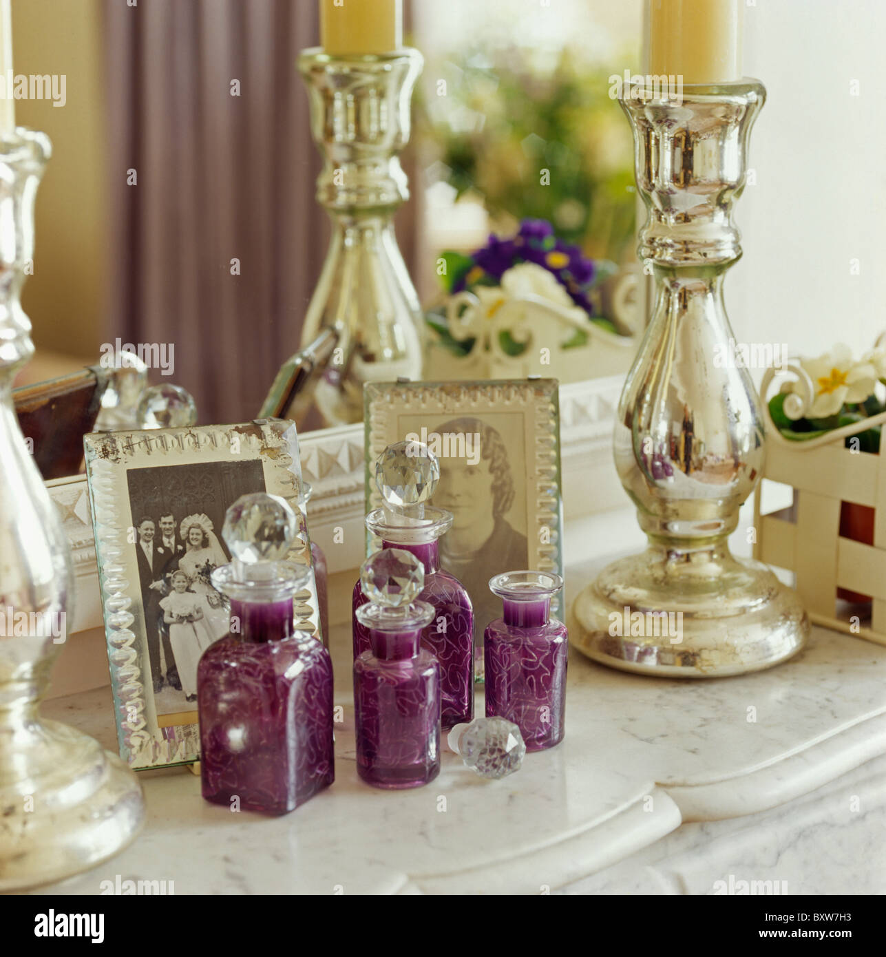 Close-up de Flacons à parfum en verre violet et argent bougeoirs sur la cheminée de marbre avec des photos Banque D'Images