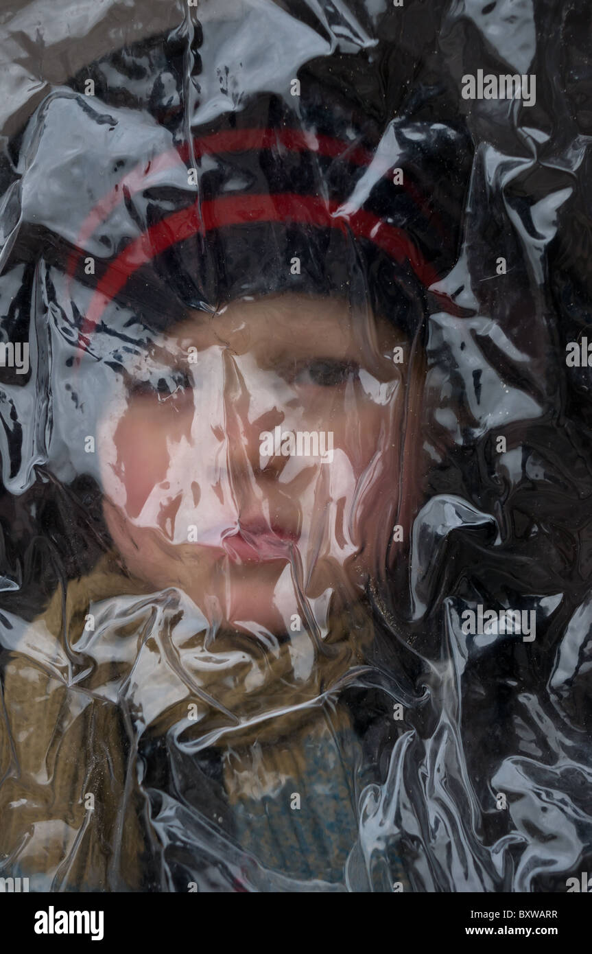 Garçon dans un chapeau d'hiver à la recherche à travers la couverture de pluie en plastique clair de son buggy ou poussette. Banque D'Images