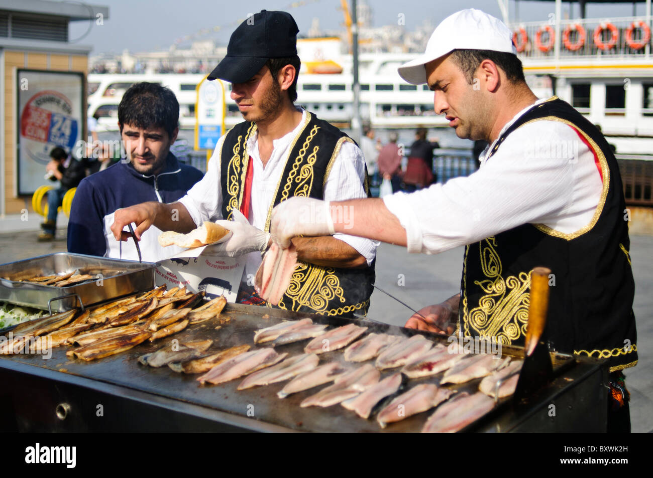 Balik Ekmek Fish Sandwich Street Food Eminonu Istanbul // ISTANBUL, Turquie — Un vendeur de rue fait griller du poisson frais sur le front de mer d'Eminonu, près du pont de Galata, préparant le traditionnel balik ekmek (sandwich au poisson). Le balik ekmek, généralement préparé avec du maquereau grillé servi dans du pain blanc avec des oignons et de la laitue, est l'un des plats de rue les plus populaires d'Istanbul. Les vendeurs de poissons riverains opèrent à partir de bateaux flottants et de stands le long de la Corne d'Or à cet endroit depuis des générations. Le quartier d'Eminonu sert de terminal de ferry majeur et de plaque tournante commerciale reliant l'Europe d'Istanbul et l'ASI Banque D'Images
