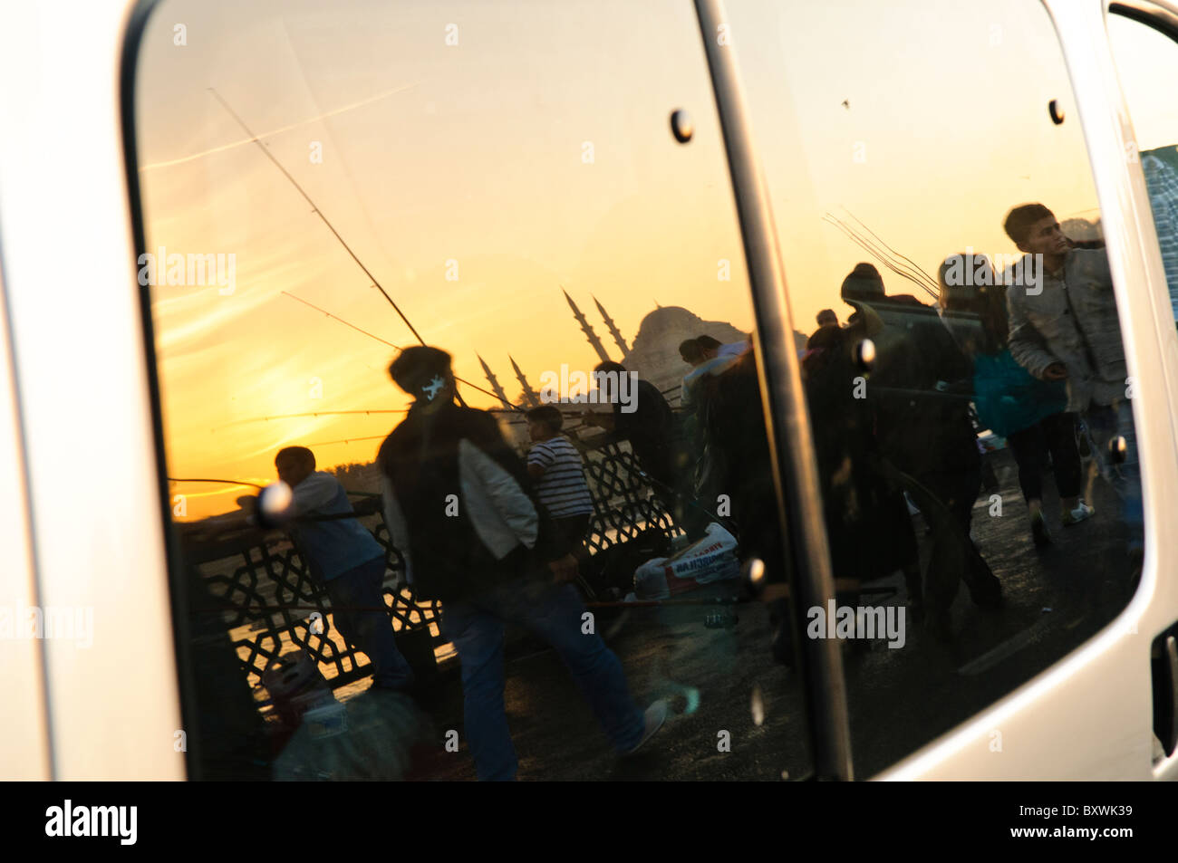 Pont de Galata réflexion des pêcheurs et de la mosquée Istanbul Turquie // ISTANBUL, Turquie — les silhouettes des pêcheurs sur le pont de Galata et le dôme de la mosquée se reflètent dans une fenêtre de voiture, créant une vue en couches sur le front de mer d'Istanbul. Le pont de Galata enjambe la Corne d'Or, reliant les quartiers historiques de Eminönü et Karaköy et constituant l'un des monuments les plus reconnaissables de la ville. Le pont est connu pour ses restaurants au niveau inférieur et les pêcheurs qui bordent sa passerelle supérieure tout au long de la journée. La Corne d'Or est un port naturel qui a été au centre de l'histo maritime d'Istanbul Banque D'Images