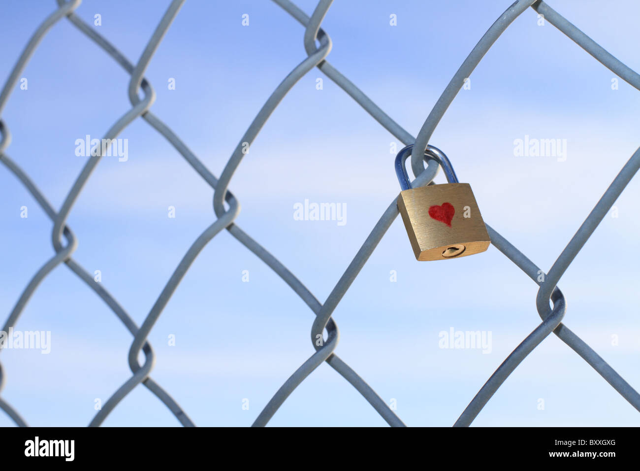 Cadenas verrouillé avec coeur suspendu à une chaîne barrière avec un ciel bleu en arrière-plan. Banque D'Images