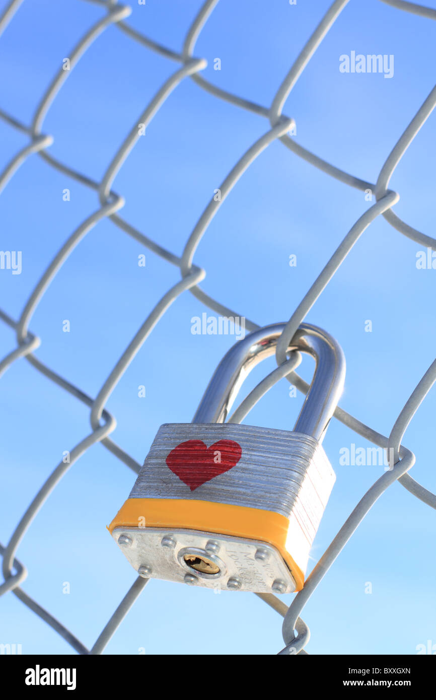 Cadenas verrouillé avec coeur suspendu à une chaîne barrière avec un ciel bleu en arrière-plan. Banque D'Images