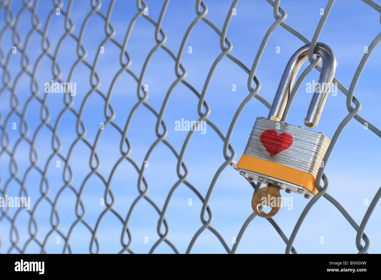 Cadenas déverrouillé avec coeur et clé suspendu à une chaîne barrière avec un ciel bleu en arrière-plan. Banque D'Images
