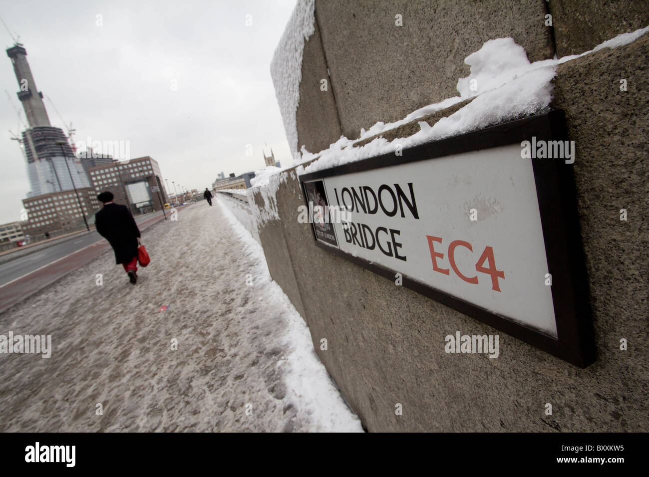 Piéton marchant sur le pont de Londres couvert de neige avec panneau de rue et la tour de verre Shard of Glass en construction sur la gauche en arrière-plan Banque D'Images