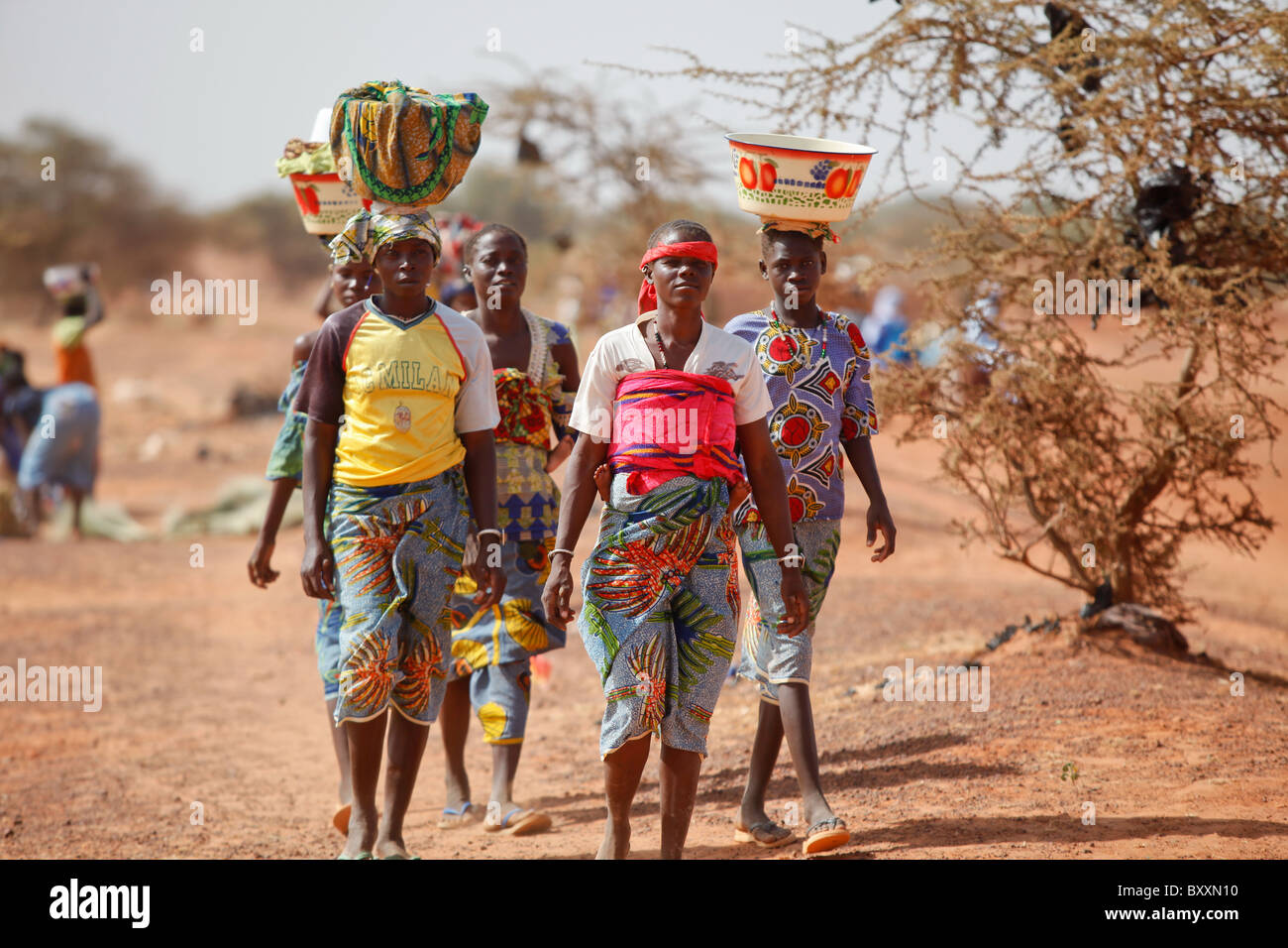 Les femmes arrivent dans la ville de Djibo, au Burkina Faso, à pied, transportant leurs marchandises sur leurs têtes à la mode traditionnelle africaine. Banque D'Images