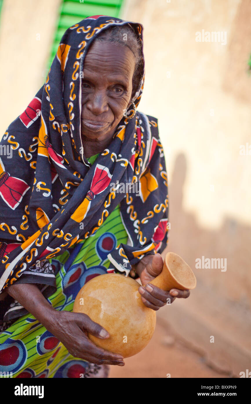 Une vieille femme Peul dans la région de la ville de Djibo dans le nord du Burkina Faso, secoue une calebasse de lait frais. Banque D'Images