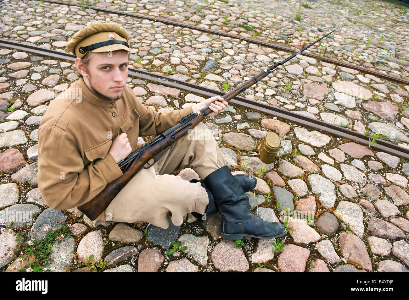 Soldat avec l'arme et de chaudière en uniforme de la Première Guerre mondiale, s'asseoir et se reposer sur la chaussée. Les temps de l'accord de costume World W Banque D'Images