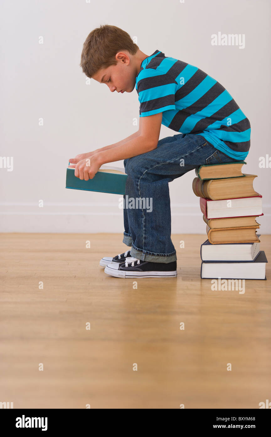 Garçon assis sur la pile de livres et lecture livre Banque D'Images