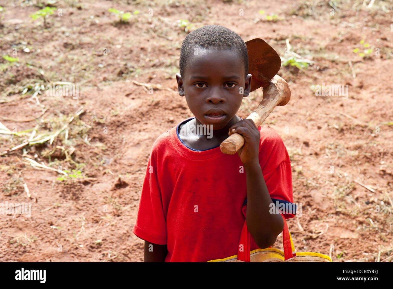 Un jeune enfant africain avec une pioche sur son devrait revient de travailler dans les champs. Banque D'Images
