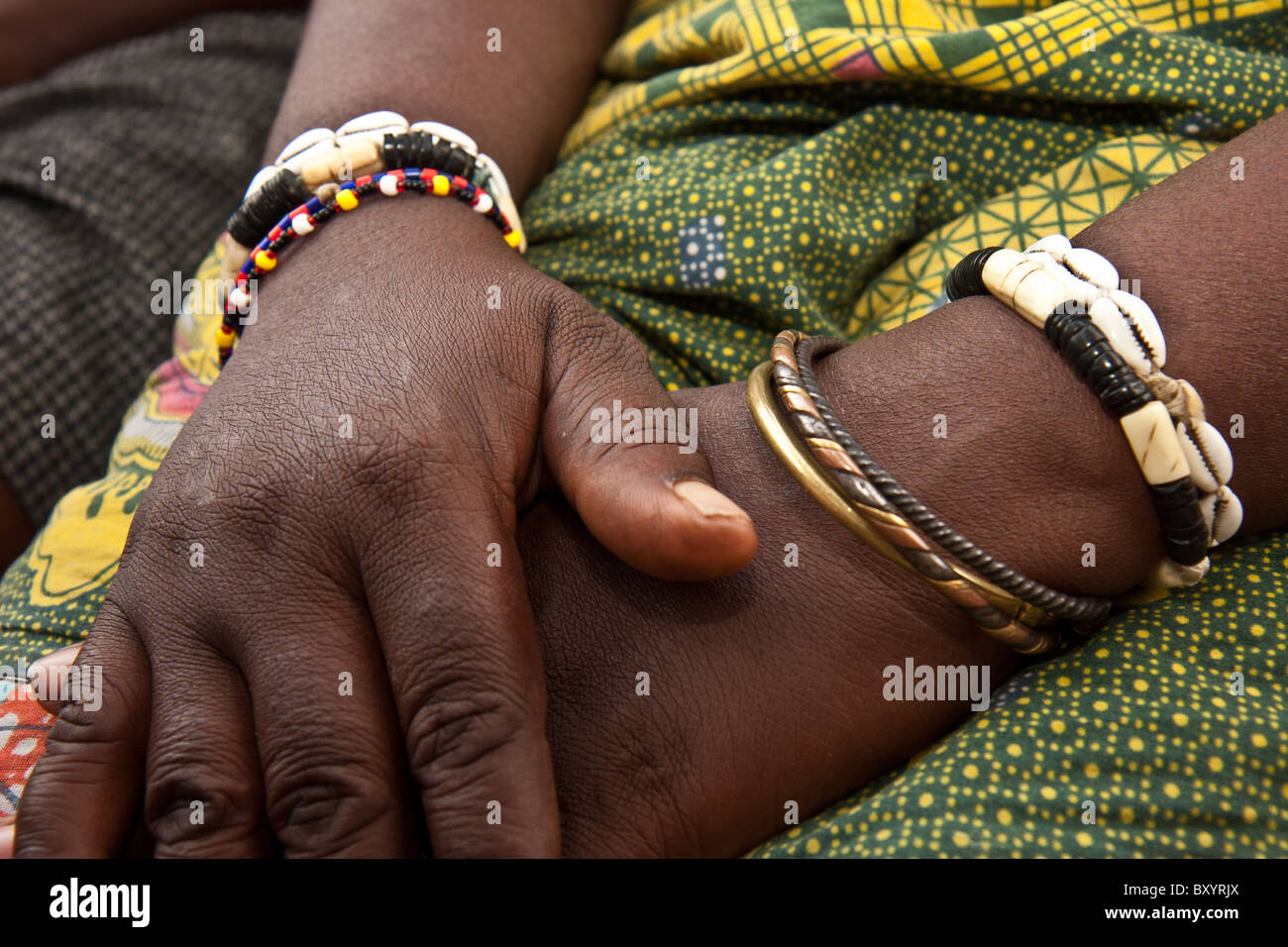 Une femme africaine se replie ses mains sur ses genoux. Bracelets traditionnels sont sur son poignet. Banque D'Images
