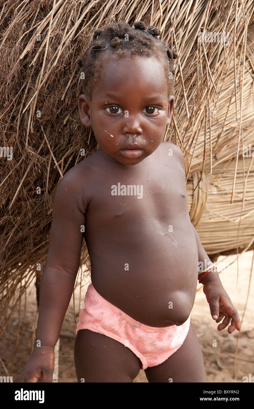 Un enfant africain se distingue avec des tas de roseaux dans l'arrière-plan. Son village a participé à un projet générateur de revenu par une ONG. Banque D'Images