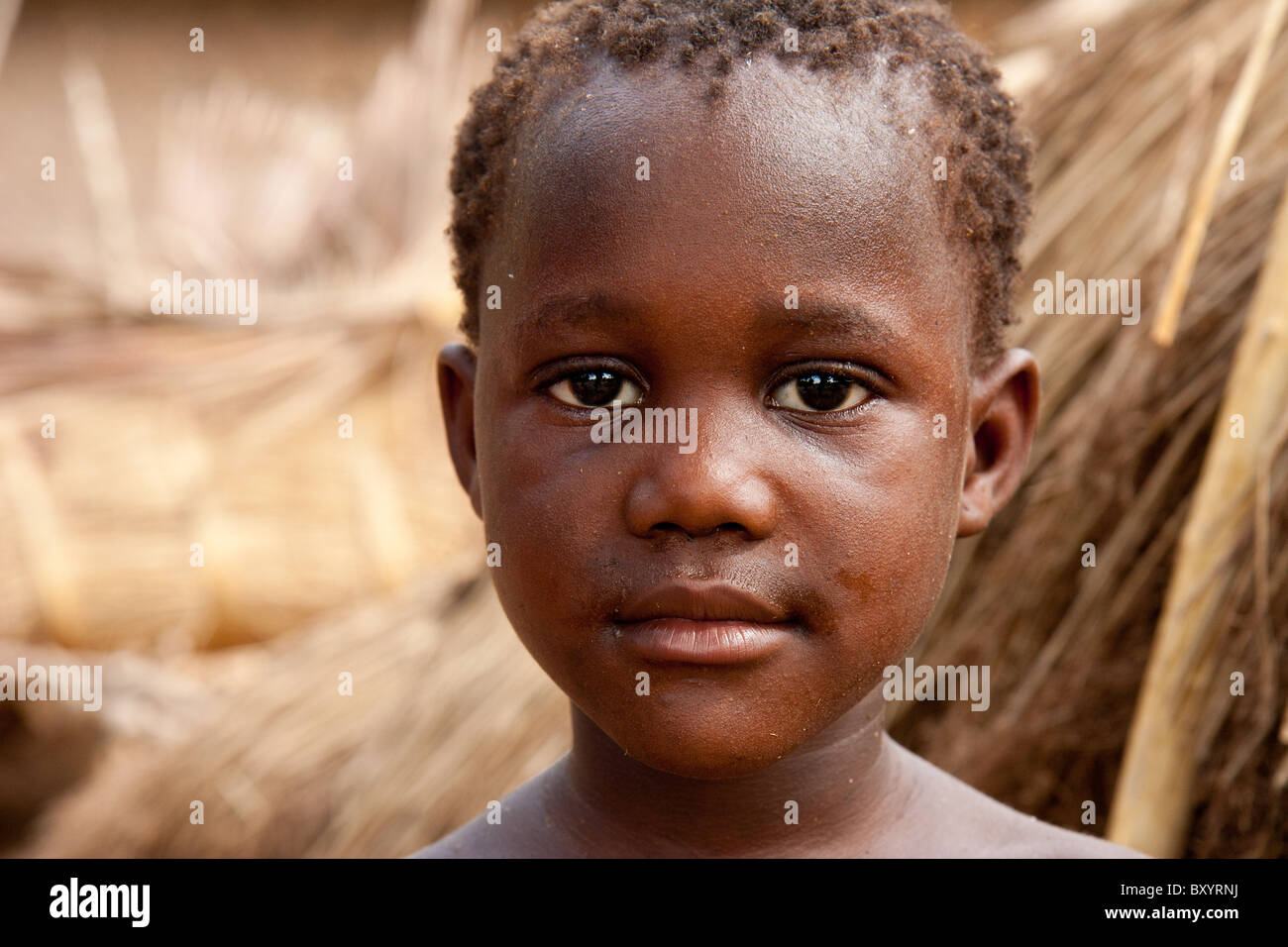 Un garçon africain se distingue avec des tas de roseaux dans l'arrière-plan. Son village a participé à un projet générateur de revenu par une ONG. Banque D'Images