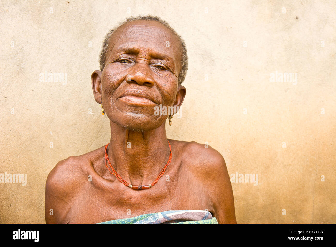 Une vieille femme africaine est assis contre un mur. La femme a participé à un projet générateur de revenu par une ONG. Banque D'Images