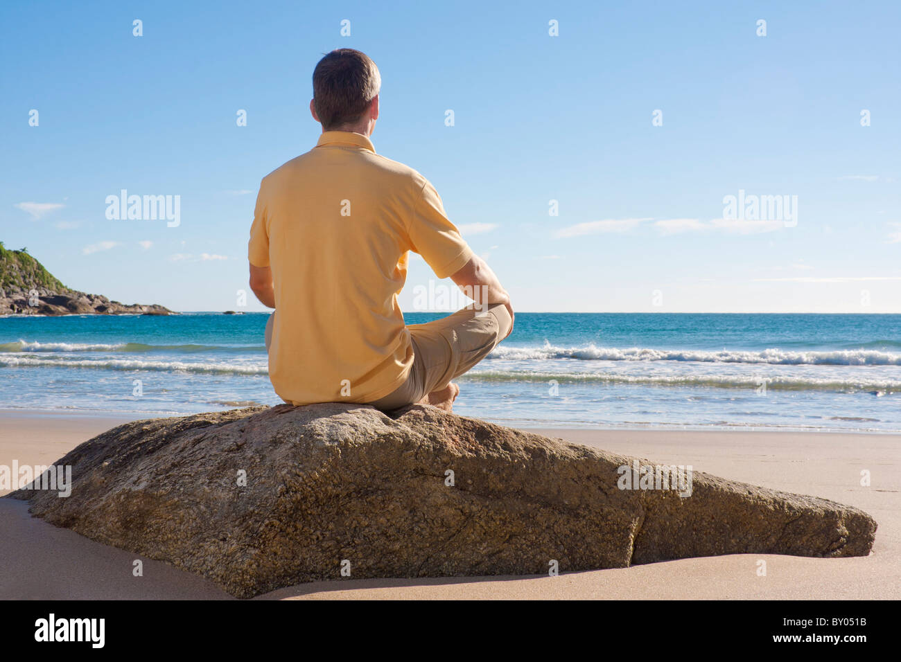 Homme assis sur un rocher à la plage et à la méditation Banque D'Images