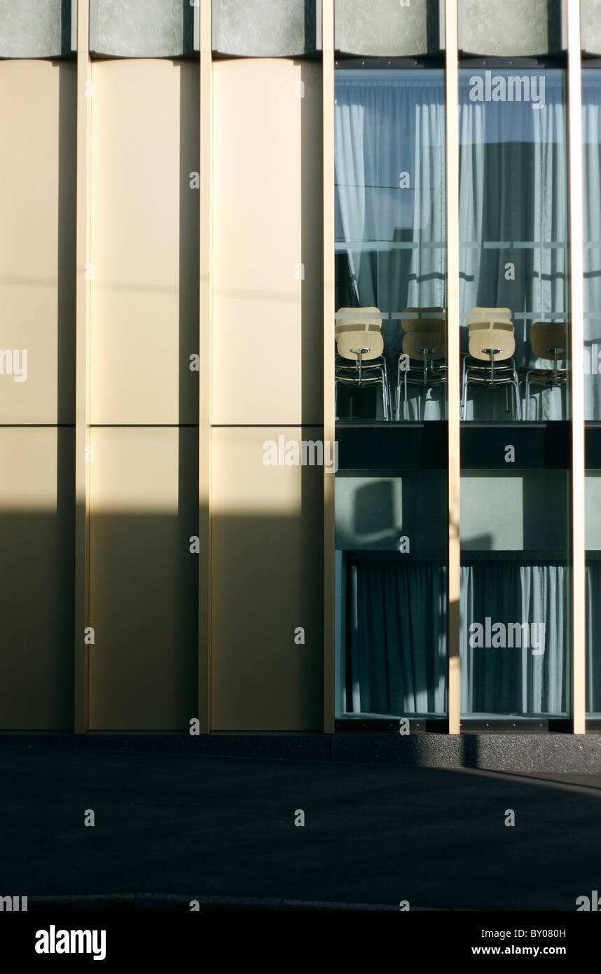 Le soleil jette une ombre sur un bâtiment avec des panneaux de verre dans une rue de la ville, avec des chaises empilées à l'intérieur de la fenêtre. Banque D'Images