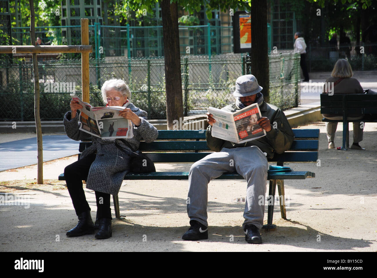 Les personnes lisant le journal sur banc de parc Paris France Banque D'Images