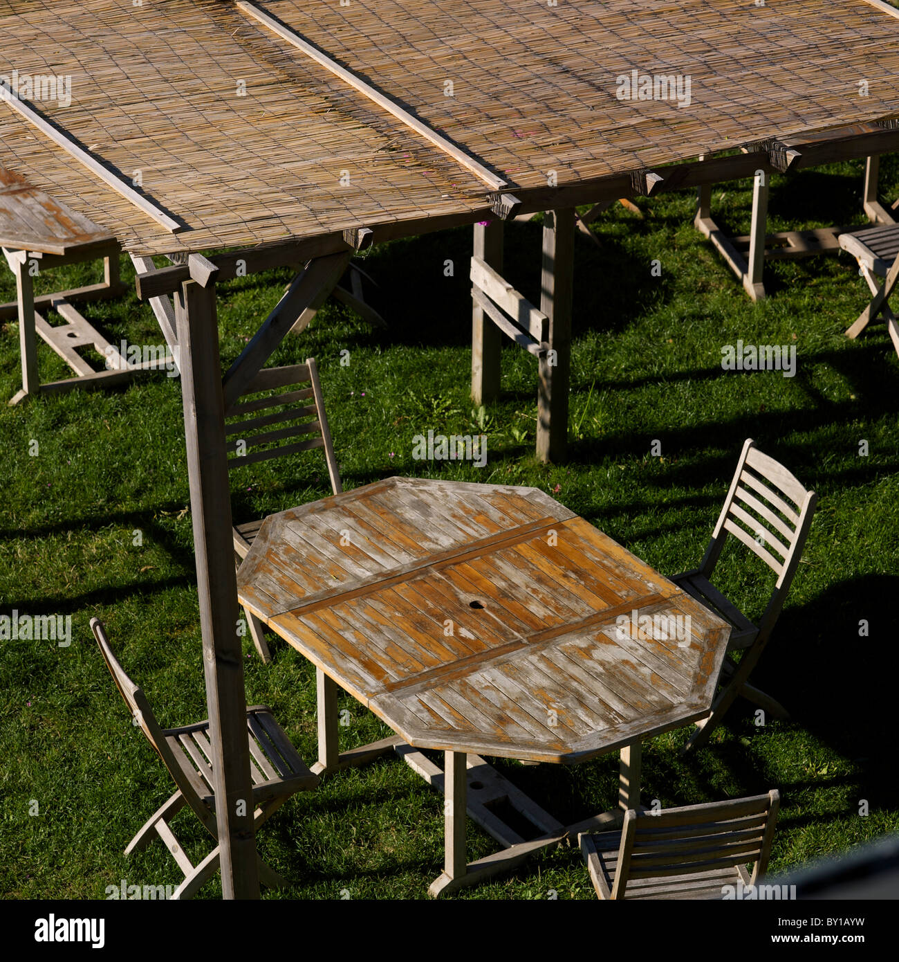 Salle à manger extérieure avec tables et chaises en bois, avec lumière naturelle et herbe verte par temps clair Banque D'Images