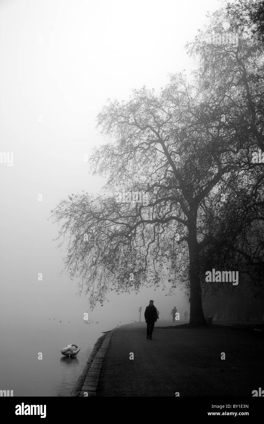 Les piétons marchant sur le côté d'un lac Serpentine, Misty, Hyde Park, London, UK Banque D'Images