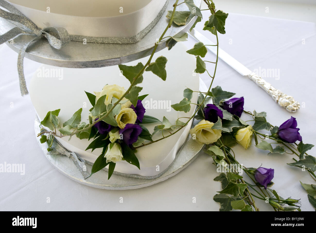 Gâteau de mariage blanc à deux vitesses drapé de pourpre et fleurs crème de lierre Banque D'Images
