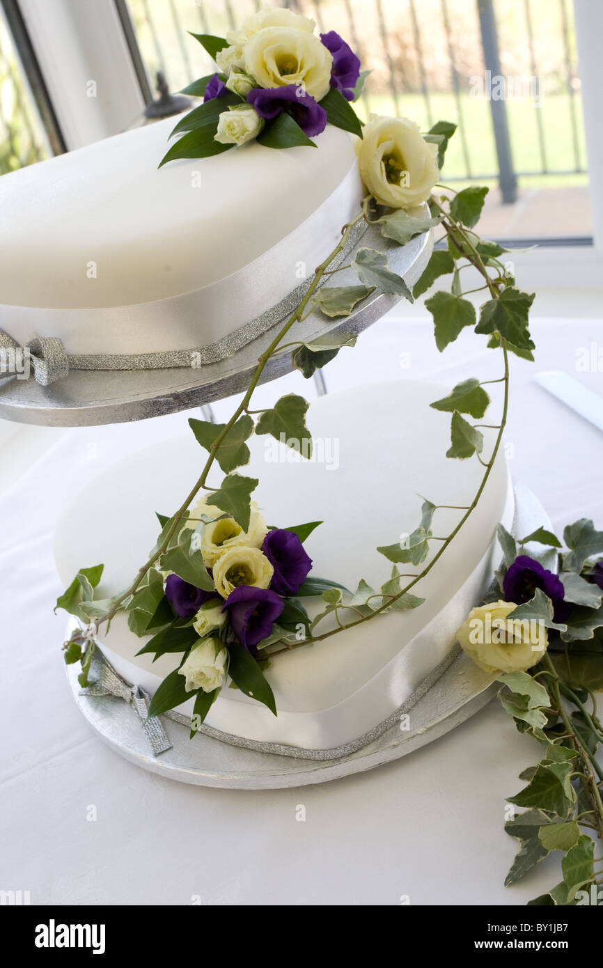 Gâteau de mariage blanc à deux vitesses drapé de pourpre et fleurs crème de lierre Banque D'Images