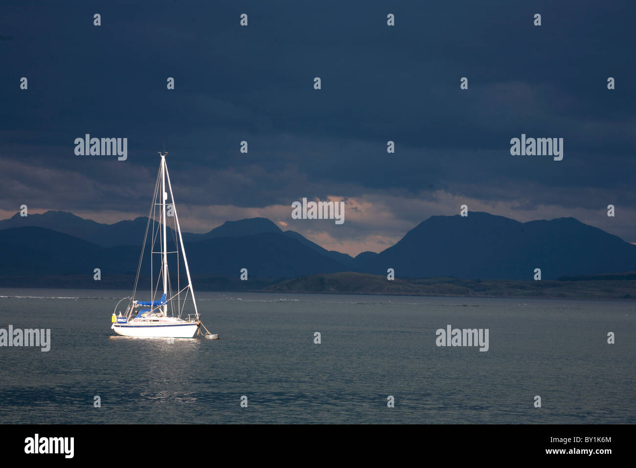 L'Écosse, l'île de Mull. Sunlit yacht dans le Sound of Mull dramtic contre un ciel d'orage. Banque D'Images