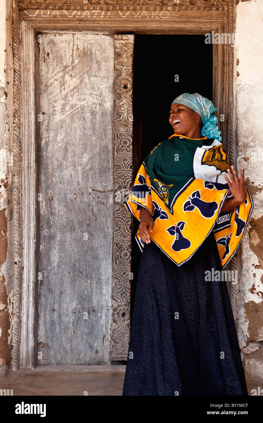 Une femme joviale au traditionnel bois sculpté porte de sa maison à Kaole, au nord de Dar-es-Salaam. Banque D'Images