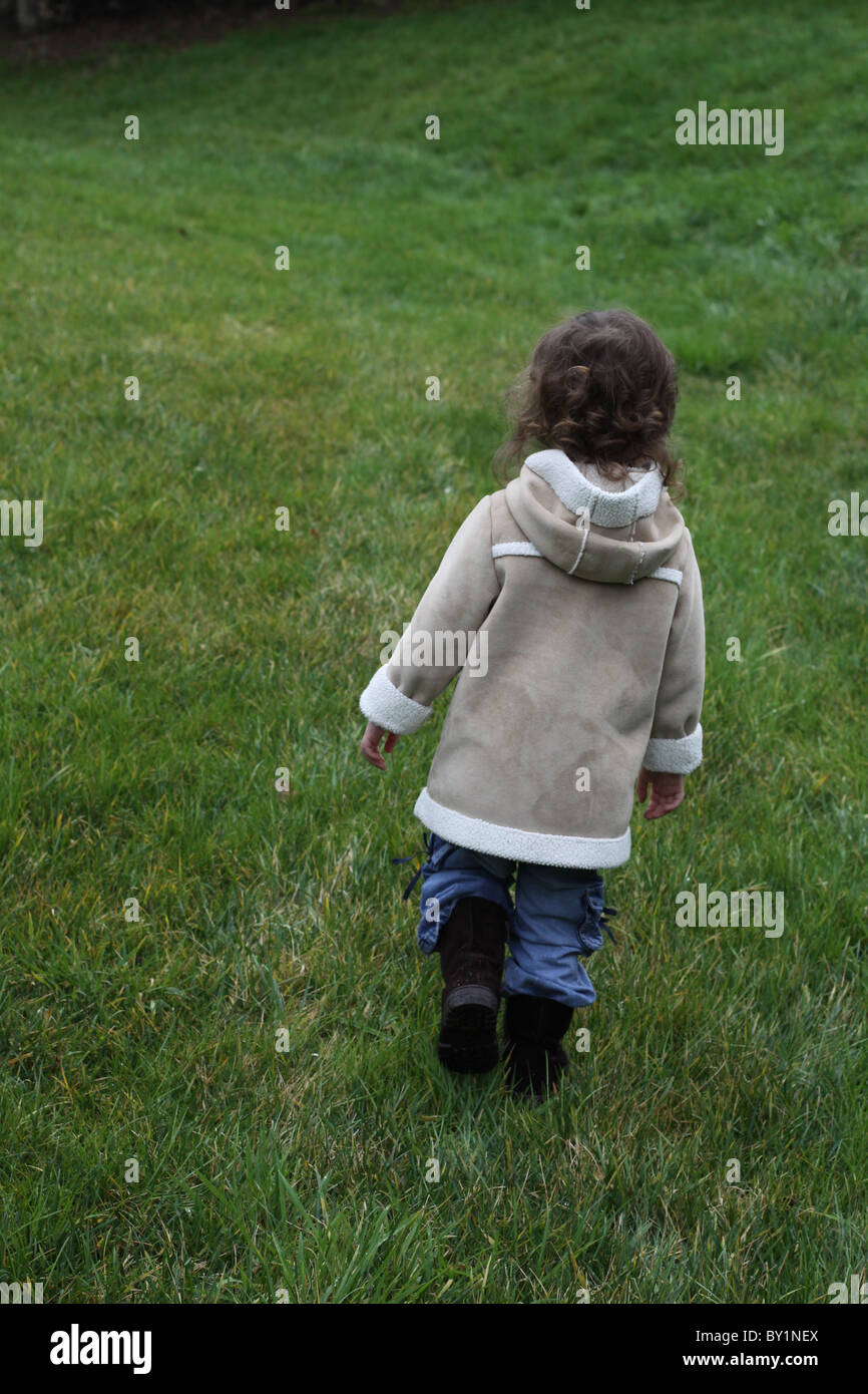 Un petit enfant qui marche dans un champ d'herbe verte. Banque D'Images