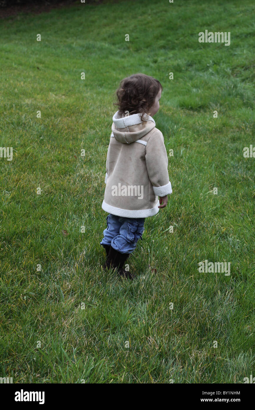 Une petite fille debout dans un champ de hautes herbes vertes et à la recherche dans la distance. Banque D'Images