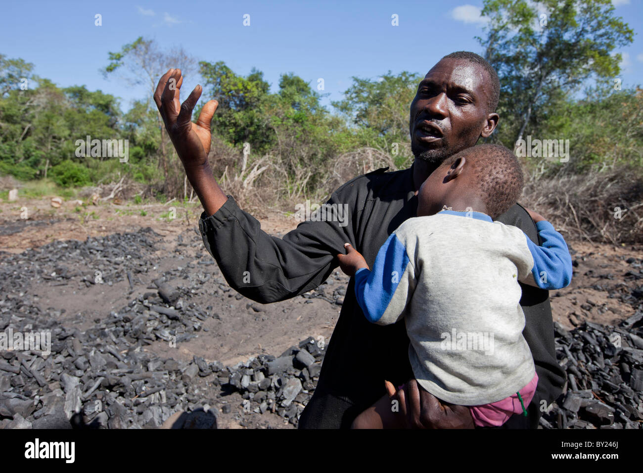 MAPUTO, Mozambique, mai 2010 : un producteur de charbon tient son fils comme il parle aux chercheurs. Banque D'Images