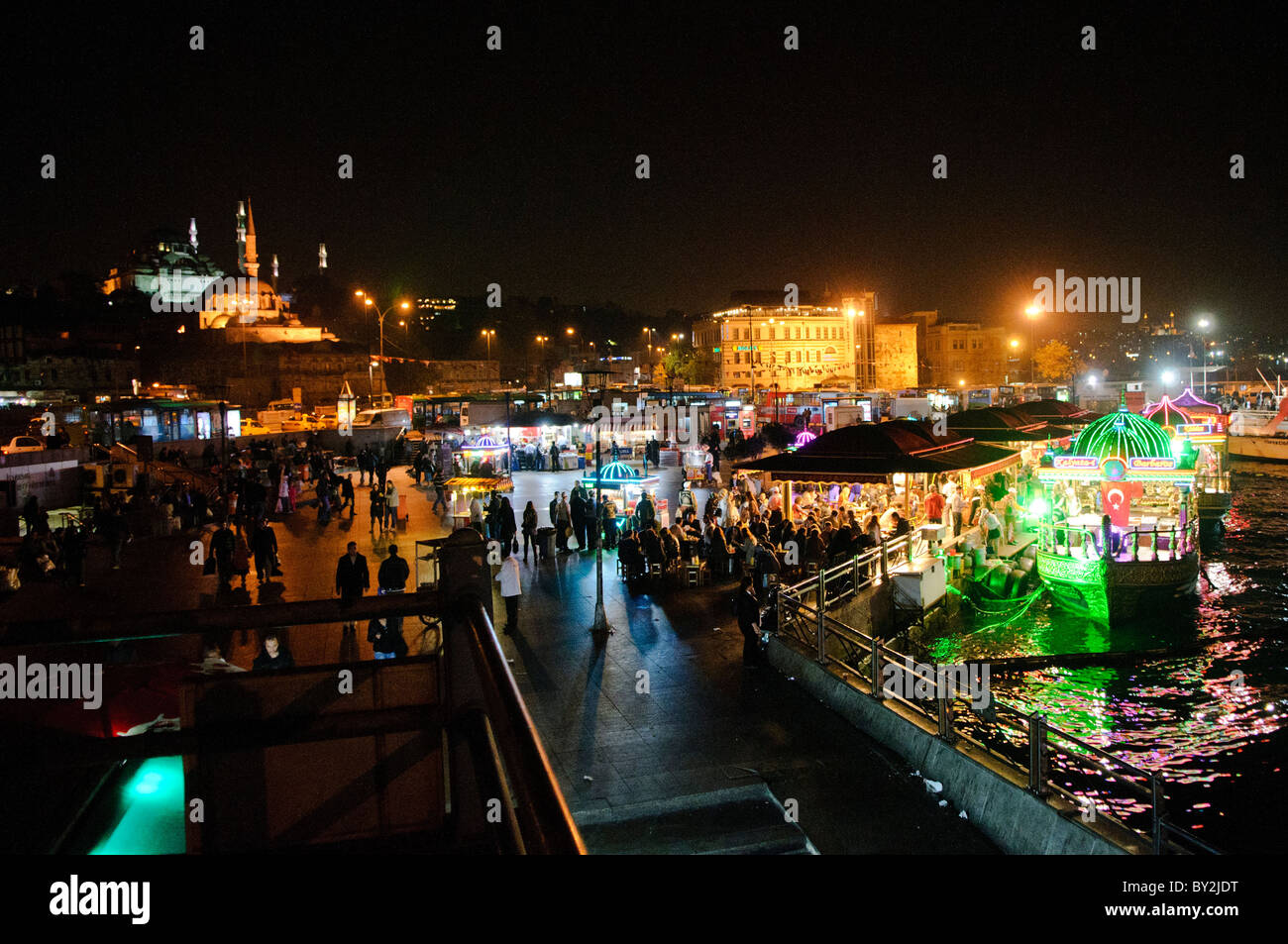 Balik Ekmek Fish Sandwich Boats Eminonu Istanbul // ISTANBUL, Turquie — les bateaux éclairés balik ekmek servent des sandwichs de poisson traditionnels aux convives le long du front de mer d'Eminonu près du pont de Galata. Ces restaurants flottants, connus localement sous le nom de balıkçı tekneleri, proposent du maquereau grillé servi dans du pain blanc avec des oignons et de la laitue comme nourriture de rue populaire. Les bateaux richement décorés présentent des motifs de style ottoman et restent amarrés en permanence le long du front de mer historique de la Corne d'Or. Eminonu sert de terminal de ferry majeur et de quartier commercial reliant les côtés européen et asiatique de l'ISTA Banque D'Images