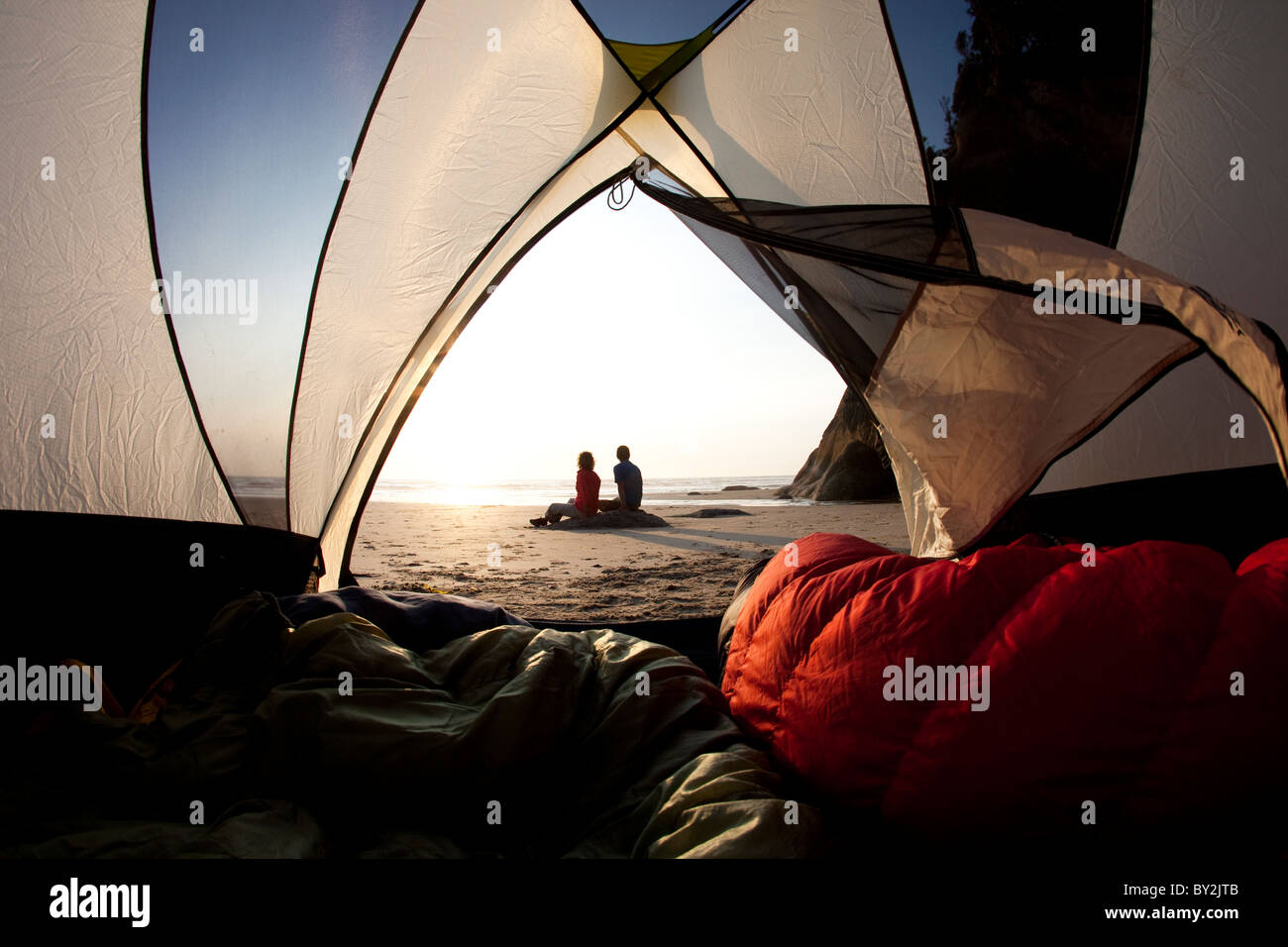 Silhouette d'un couple mâle et femelle sur la plage encadrée de leur tente en admirant le coucher du soleil. Banque D'Images