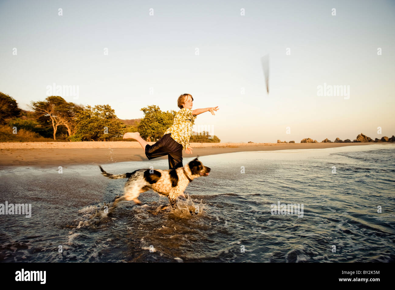 Un jeune garçon joue fetch avec son chien, au coucher du soleil sur une plage au Mexique. Banque D'Images