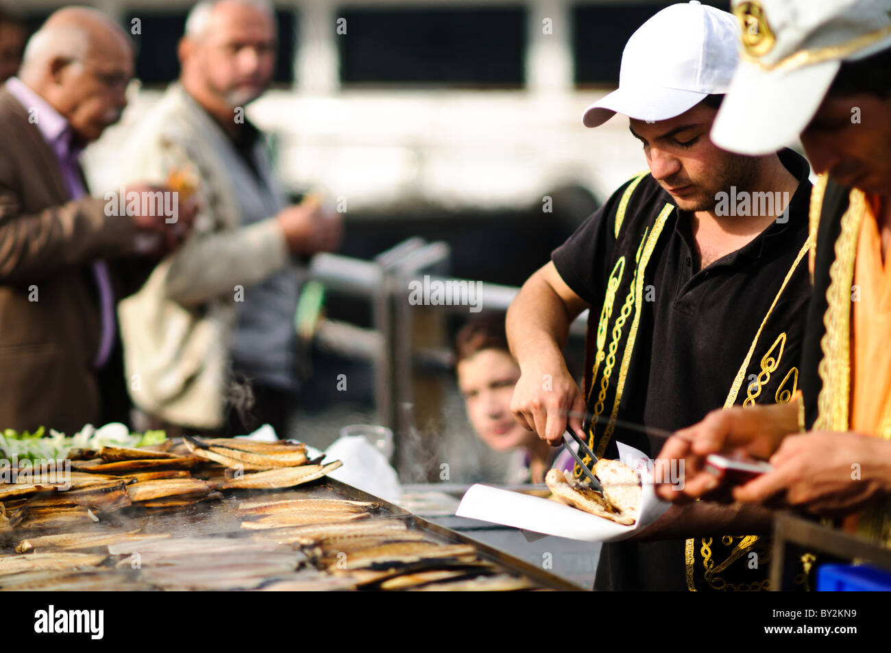 Balik Ekmek Fish Sandwich Street Food Istanbul Turquie // ISTANBUL, Turquie — Un vendeur de rue grillera du poisson frais sur le front de mer d'Eminonu, près du pont de Galata, préparant le traditionnel balik ekmek (sandwich au poisson). Le balik ekmek, généralement préparé avec du maquereau grillé servi dans du pain blanc avec des oignons et de la laitue, est l'un des plats de rue les plus populaires d'Istanbul. Les vendeurs de poissons riverains opèrent à partir de bateaux flottants et de stands le long de la Corne d'Or à cet endroit depuis des générations. Le quartier d'Eminonu sert de terminal de ferry majeur et de plaque tournante commerciale reliant l'Europe et l'Asie d'Istanbul Banque D'Images