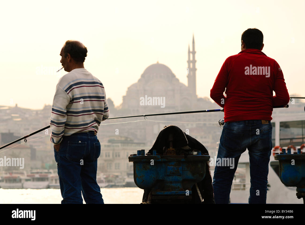 Pêcheurs pêchant la mosquée Suleymaniye de la Corne d'Or Istanbul Turquie // ISTANBUL, Turquie — les pêcheurs jettent leurs lignes depuis le front de mer près du marché aux poissons de Karakoy le long de la Corne d'Or. Le pont historique de Galata, un lieu de pêche populaire, relie les quartiers de Karakoy et Eminonu. L'emblématique mosquée Suleymaniye, achevée en 1557 sous l'Empire ottoman, domine l'horizon. Banque D'Images