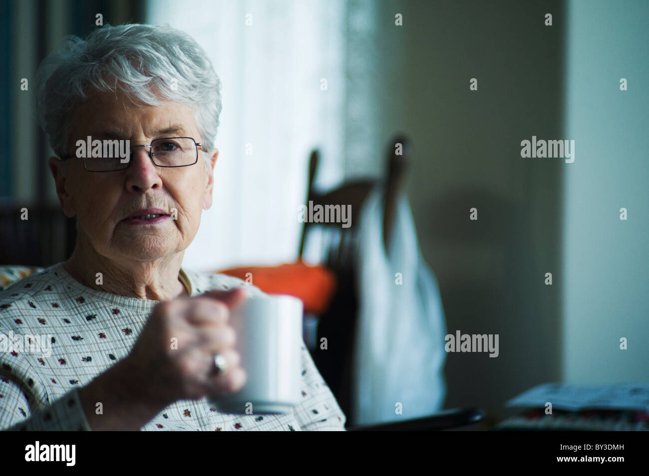 Vieille Femme est titulaire d'une tasse de thé et regarde avec inquiétude au photographe. Banque D'Images