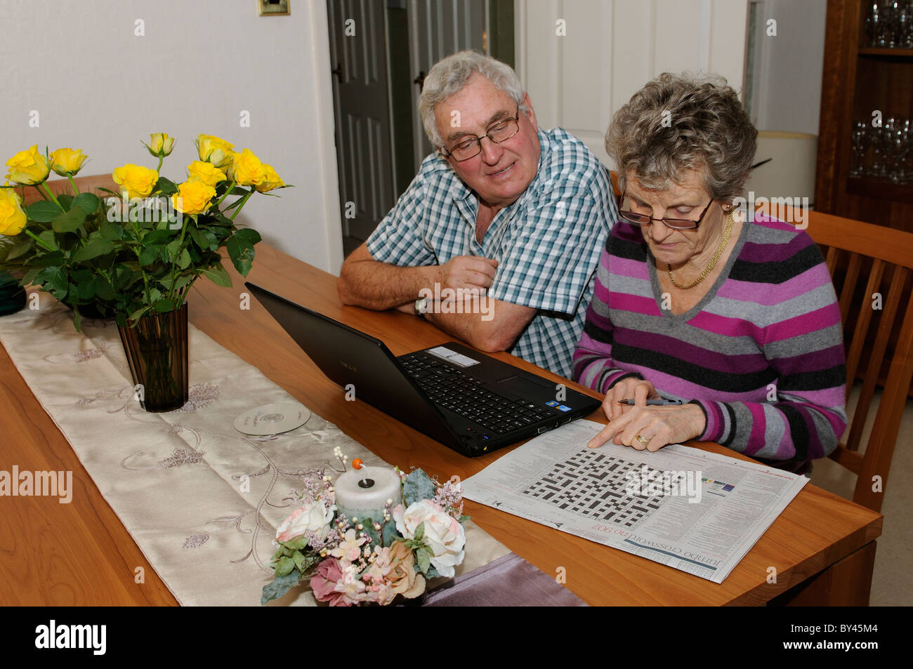 Couple de personnes âgées à l'aide de la résolution des problèmes de mots croisés leur ordinateur portable et Internet à partir de leur salon Banque D'Images