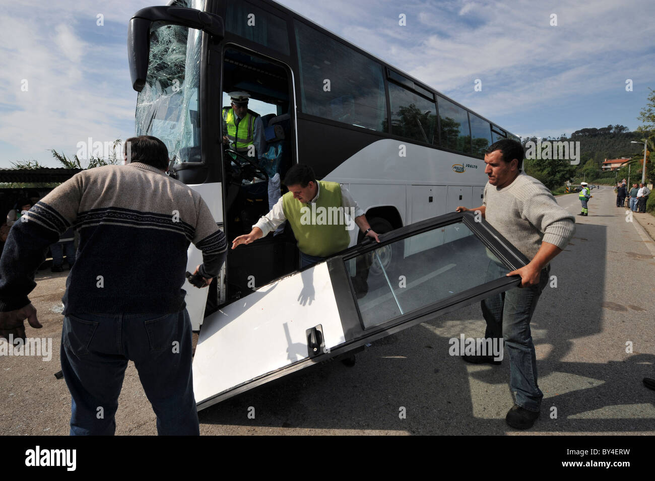 Trois hommes prendre la porte de l'épave d'un bus avec verre de pare-brise en éclats après un accident de voiture Banque D'Images
