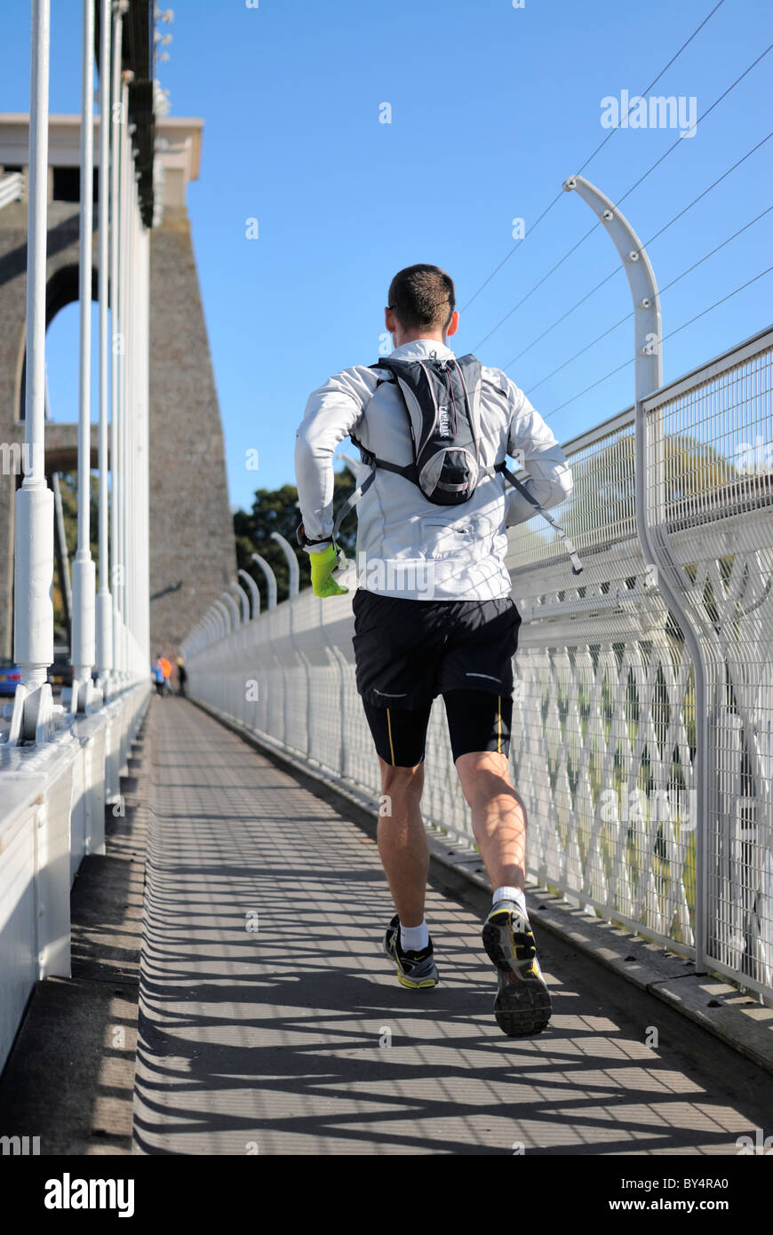 Un jogging mâle traversant le célèbre pont suspendu Clifton de Bristol lors d'une belle matinée ensoleillée. Banque D'Images