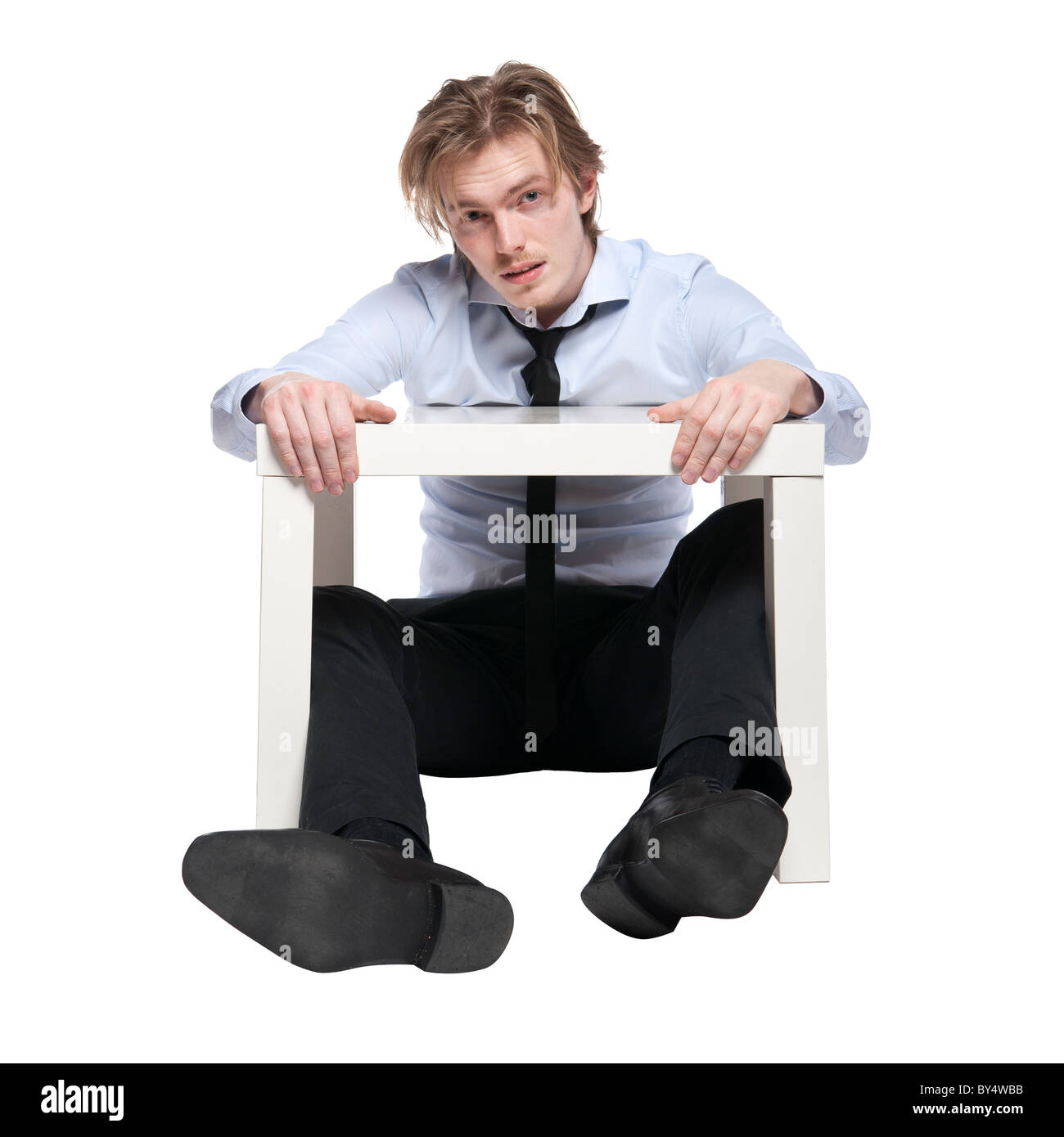 Jeune homme d'affaires, de travailleur ou étudiant assis à drôle de petite table. Studio photo, isolé. Banque D'Images