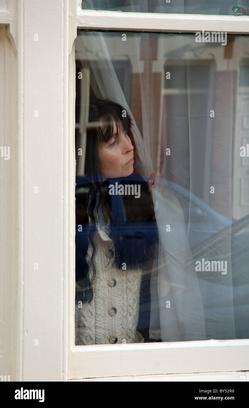 Woman peering autour de rideau, England, UK Banque D'Images