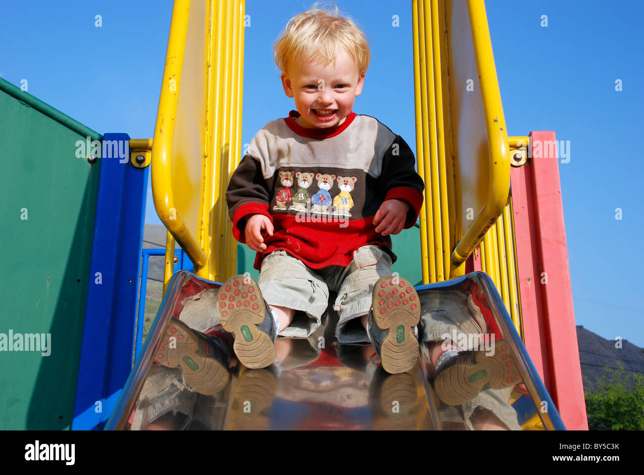 Un jeune garçon sur une diapositive dans un parc de jeu. Banque D'Images