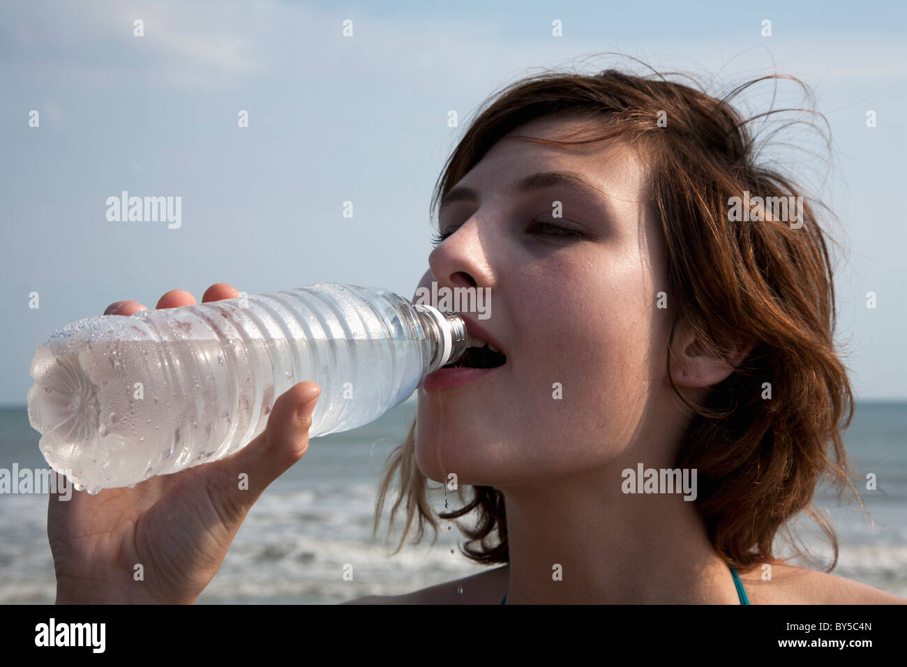 Une femme à boire de l'eau en bouteille à la plage Banque D'Images
