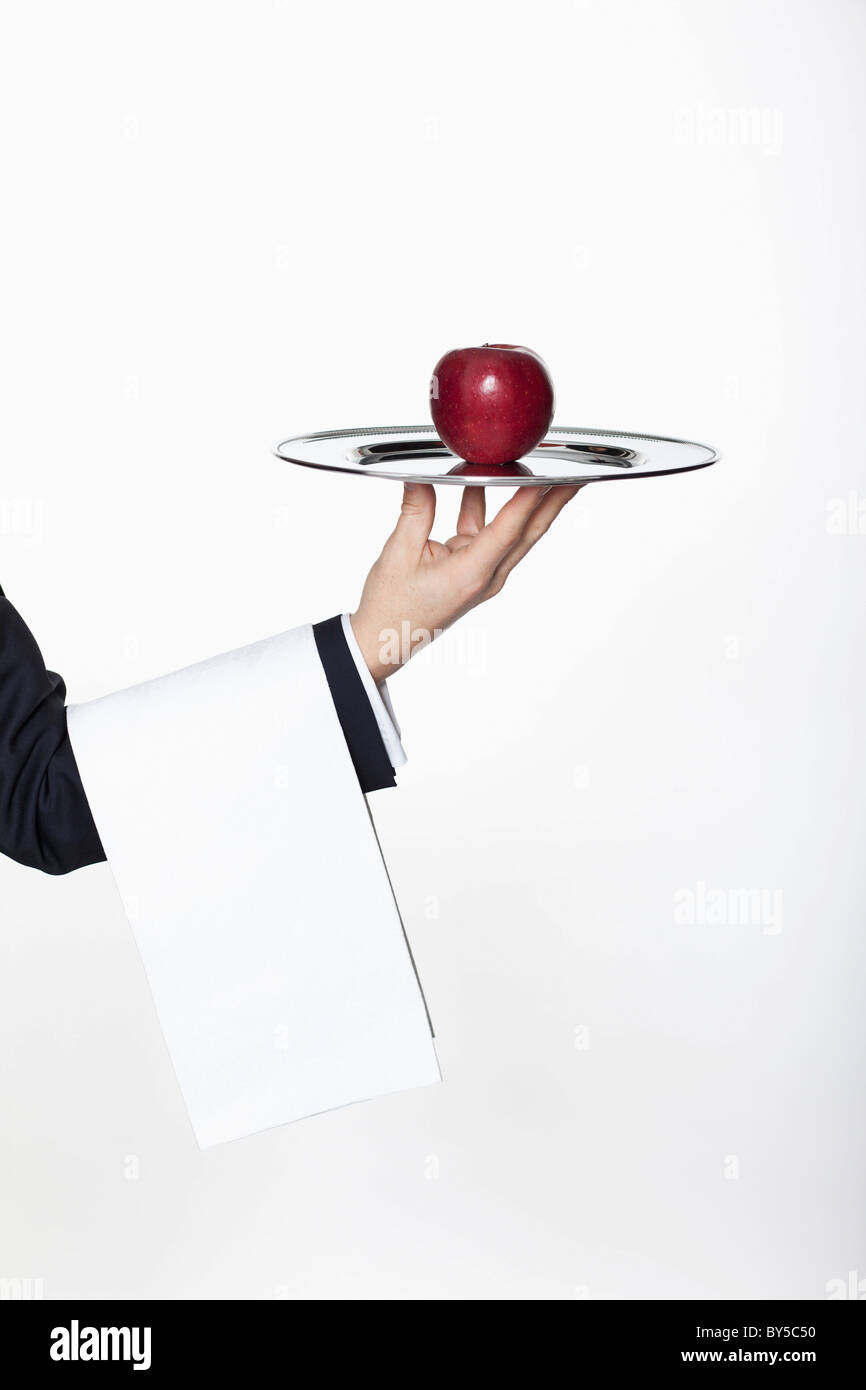 Un majordome présentant une pomme sur un plateau d'argent, focus on hand Banque D'Images